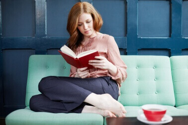 koltukta kitap okuyup kahve içen kadın
