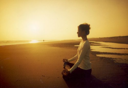 gün batımı sahilde meditasyon yapan kadın
