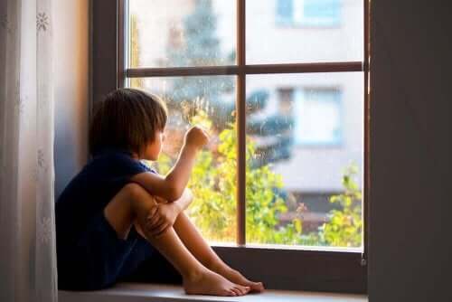 Pencerenin yanına oturmuş dışarıya bakmakta olan bir çocuk.