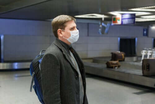 havaalanında bavul beklerken maske takmış olan adam
