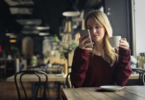 Telefonuna bakarak kahve içen bir kadın.
