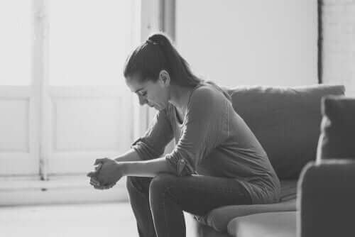 Kanepede önüne üzgün bir şekilde bakarak oturan bir kadın.