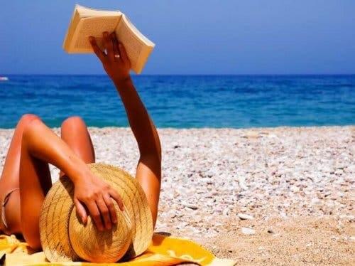 Plajda güneşlenerek kitap okuyan bir kadın.