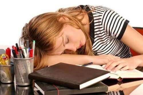 Önündeki kitapların üzerinde uyumuş yorgun bir kadın.