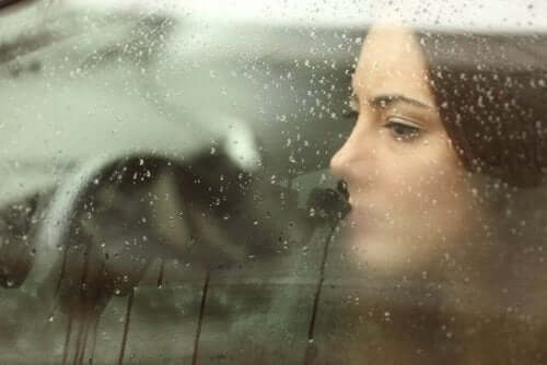 Bir kadın yağmurda buğulanmış ara camından dışarıya bakıyor, üzgün. 