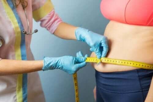 Kilolu bir kişinin karnını ölçen bir doktor.