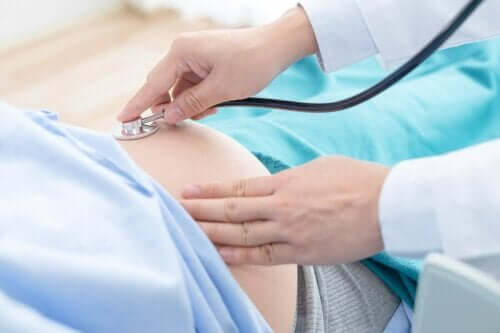 Bir doktor hamile bir kadının göbeğini stetoskop ile muayene ediyor.
