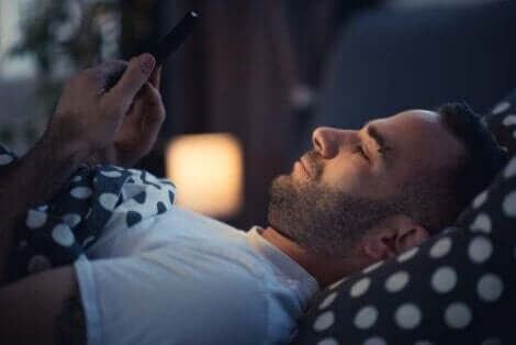 bir adam yatakta telefonuyla oynuyor